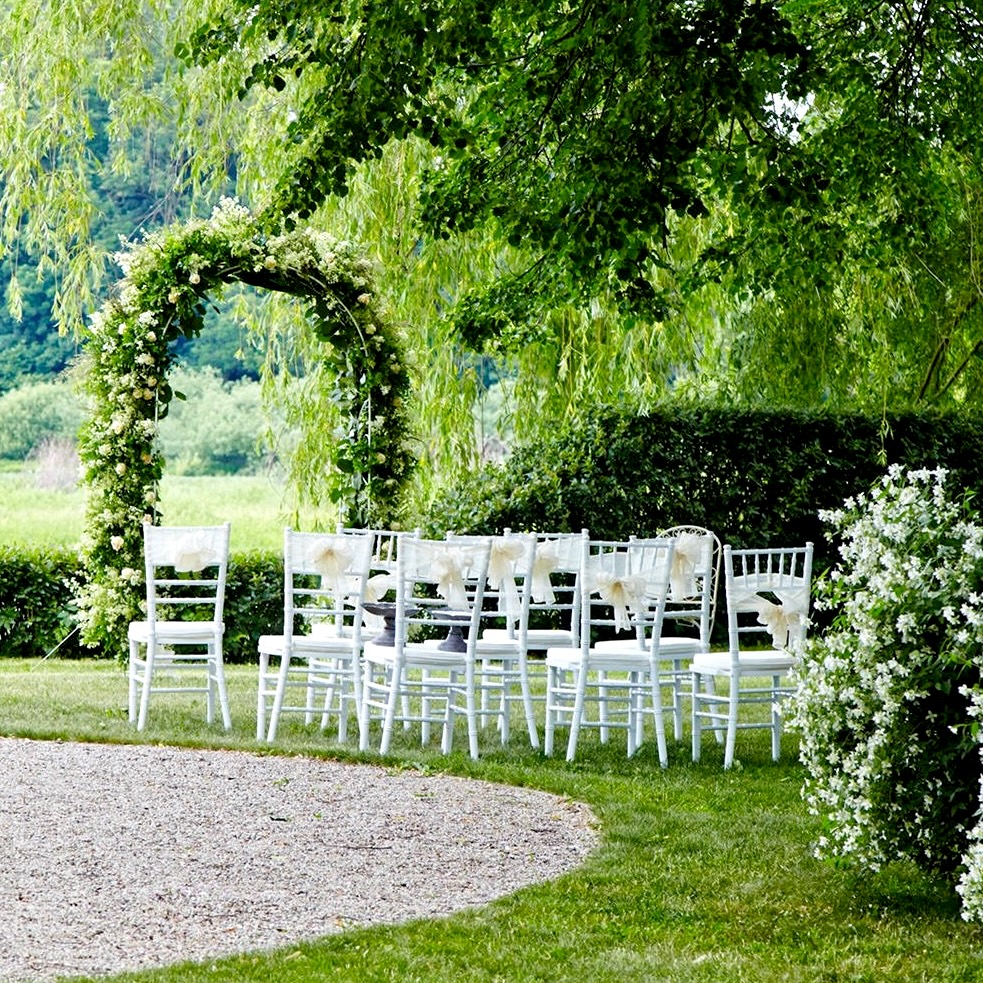 A series of white chairs set up in a grassy area next to a leafy arch
