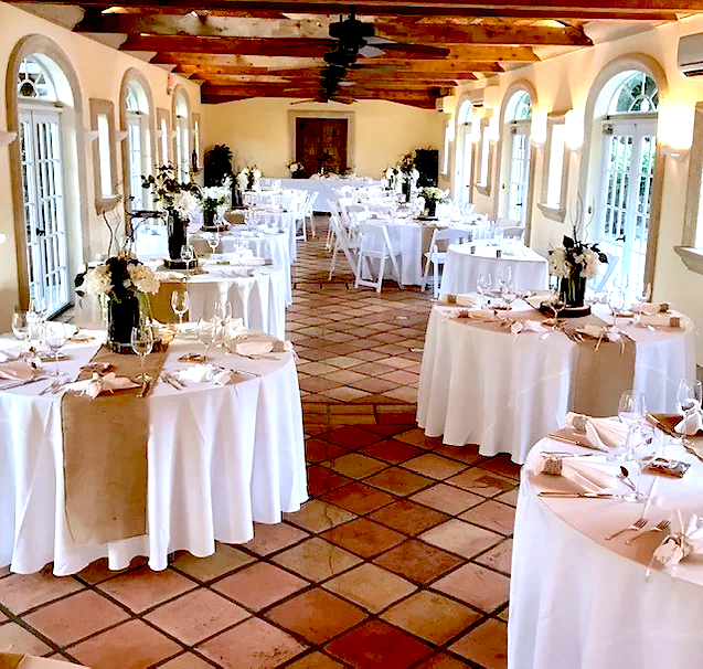 Two rows of tables covered in white tablecloths, gold runners and place settings