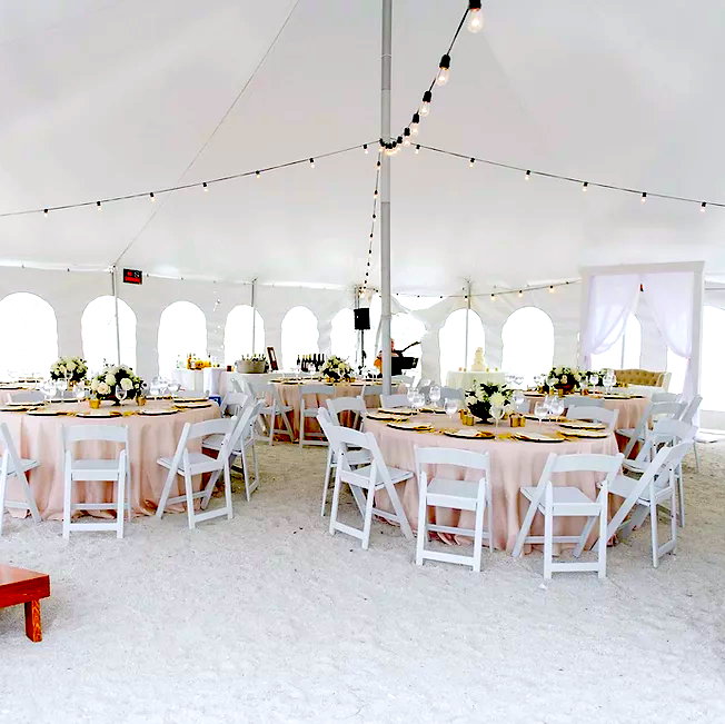 A series of tables covered in pink tablecloths and surrounded by white folding chairs, all set up under a large tent